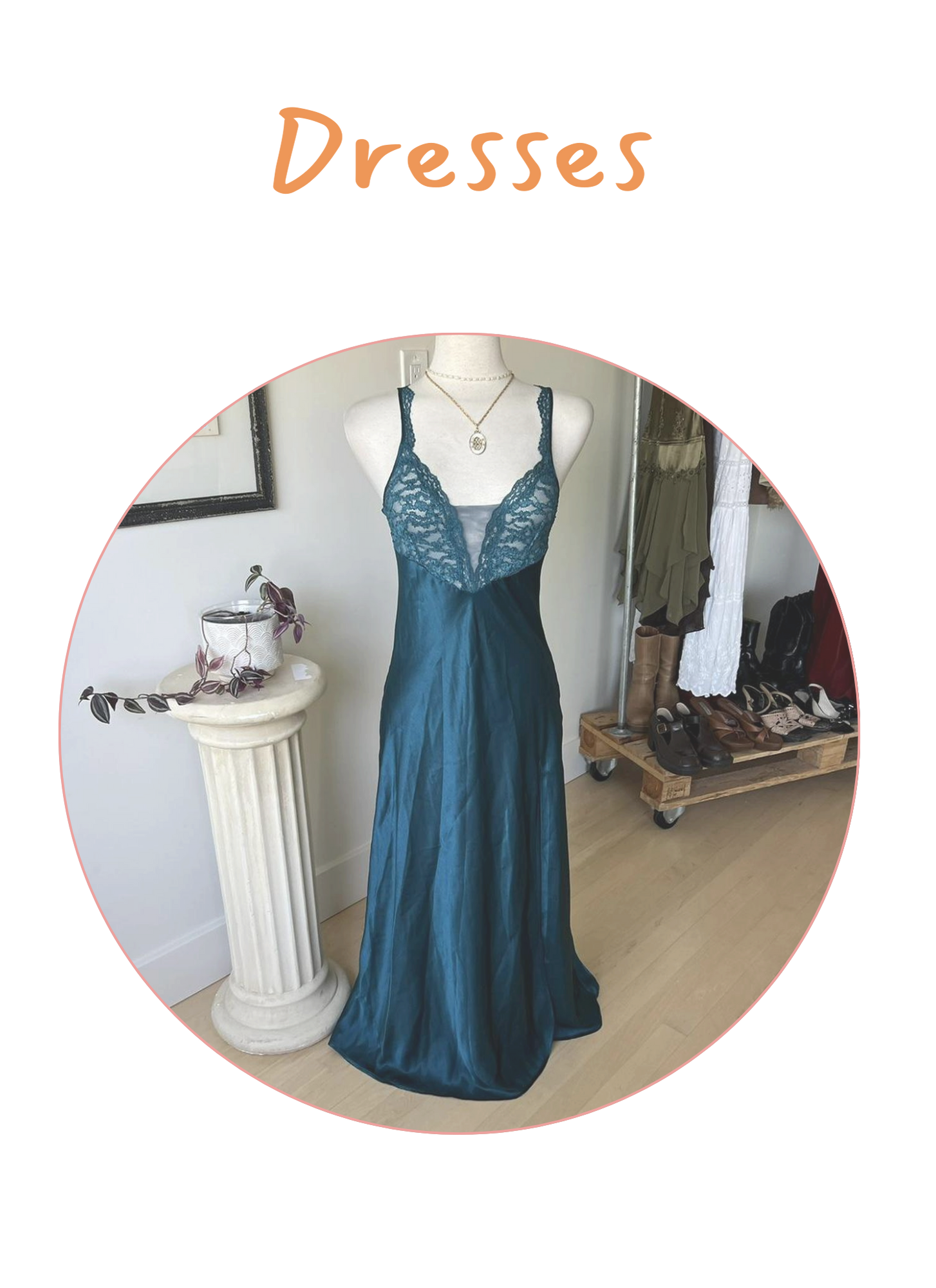 A mannequin wearing a long, teal satin slip dress with lace detailing on the bust, displayed indoors near a white pedestal with a potted plant, and a clothing rack with shoes and dresses in the background.