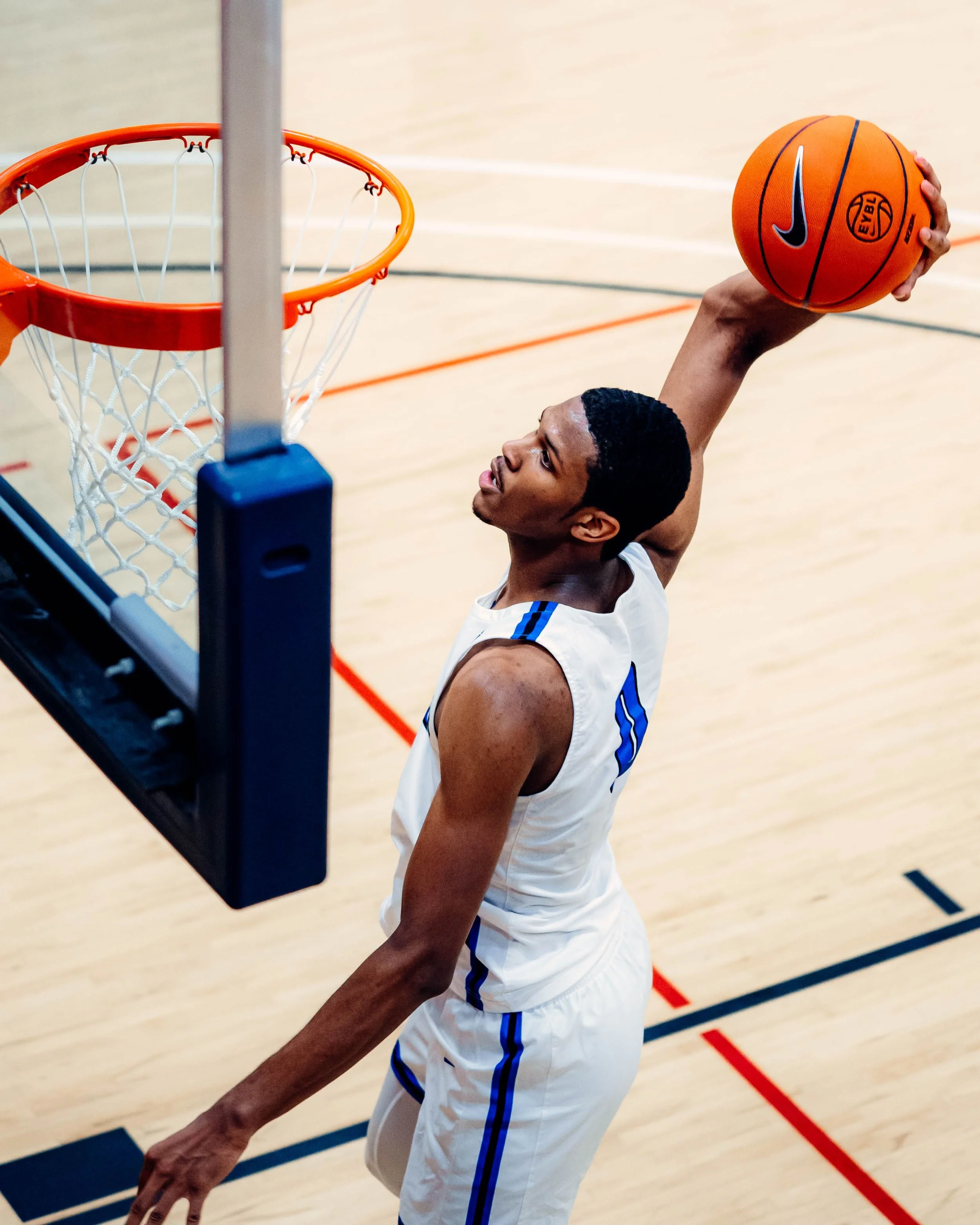 A male basketball player in a white jersey is jumping towards the hoop to dunk a basketball during a game.