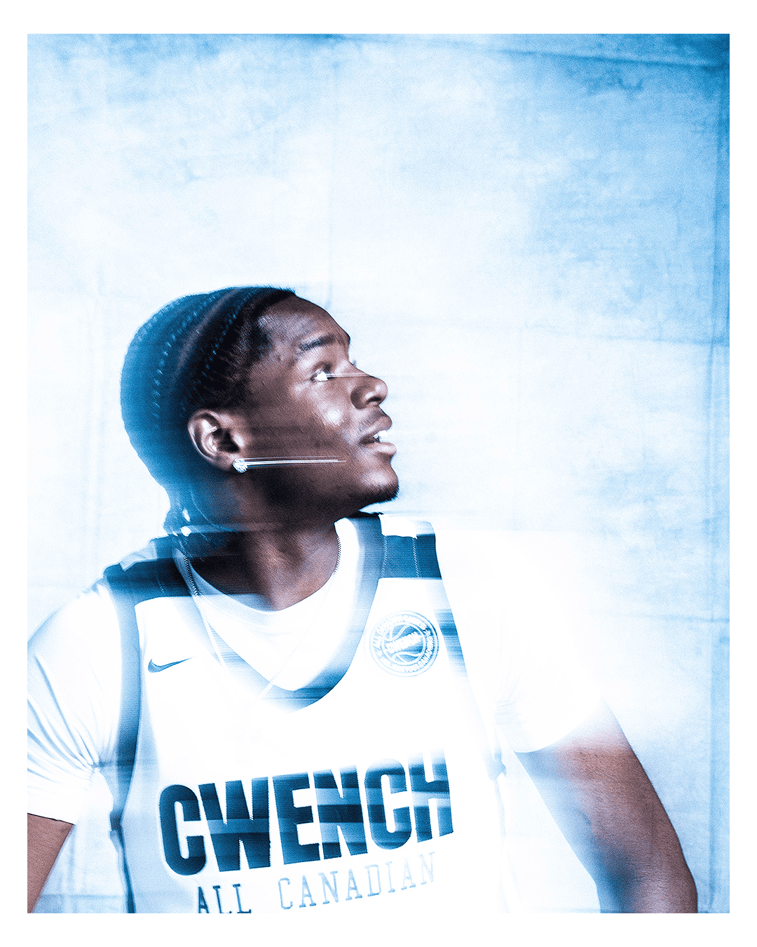 Portrait of a young male athlete with dreadlocks wearing a white sports jersey with the word 'CWECH' and 'ALL CANADIAN' written on it, looking upward.
