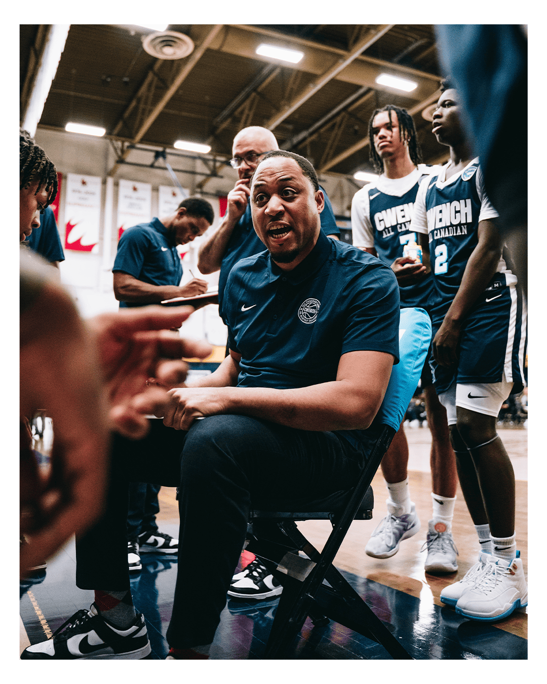 Coaching staff giving instructions to basketball players during a timeout in a gymnasium.