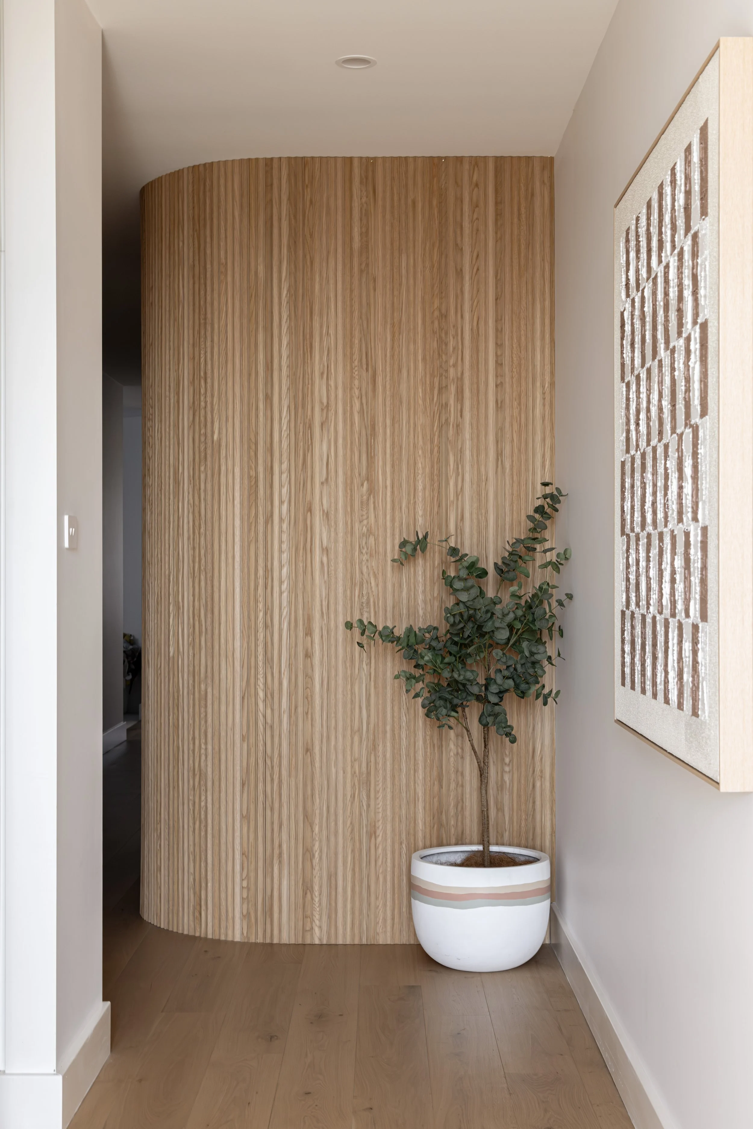 Indoor corner with a potted tree, wooden wall, and framed art.