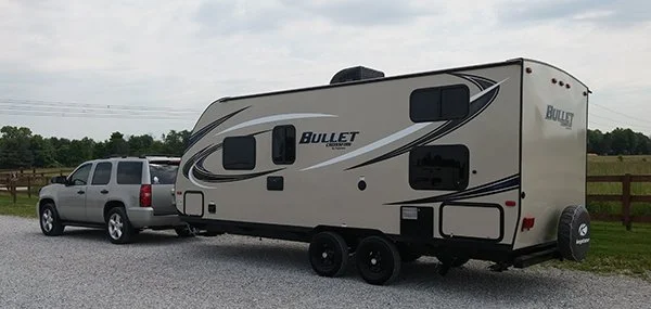 A Tahoe hauling a Keystone Bullet travel trailer parked on the side of the road.  The picture is taken from the side, but more behind the rig.