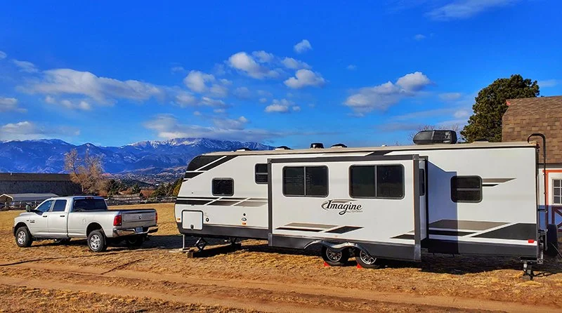 A Grand Design 3000QB with a truck disconnected sitting in front of it with mountains in the background and very blue sky with a few scattered clouds.