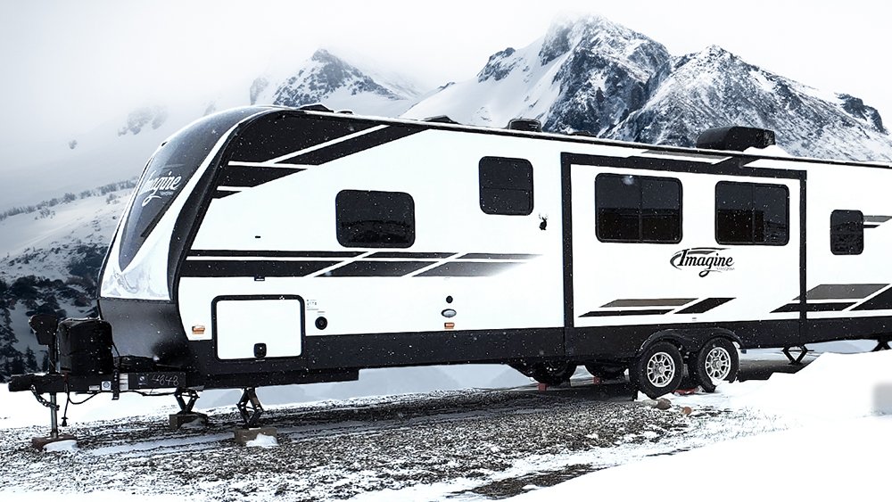 A Grand Design 3000QB sitting in a winter wonderland.  There is snow in the foreground and snowy mountains in the background.