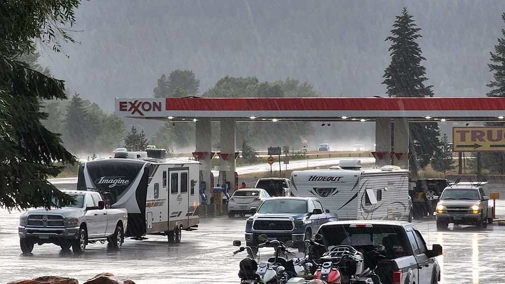 A gas station in the background while it is pouring rain. Two RVs and other cars are in the foreground.