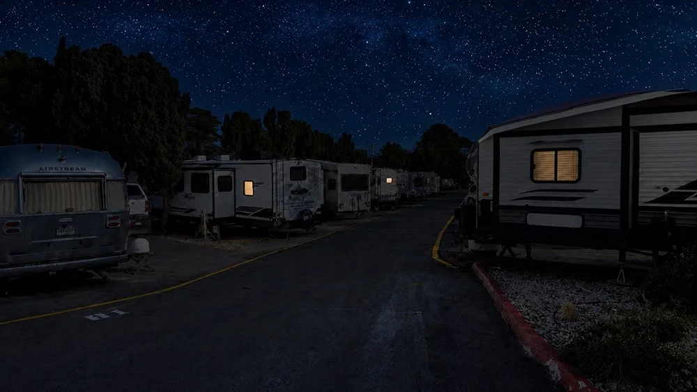 A stary night at a dimly-lit campground with dozens of RVs extending into the distance down a this paved isle.