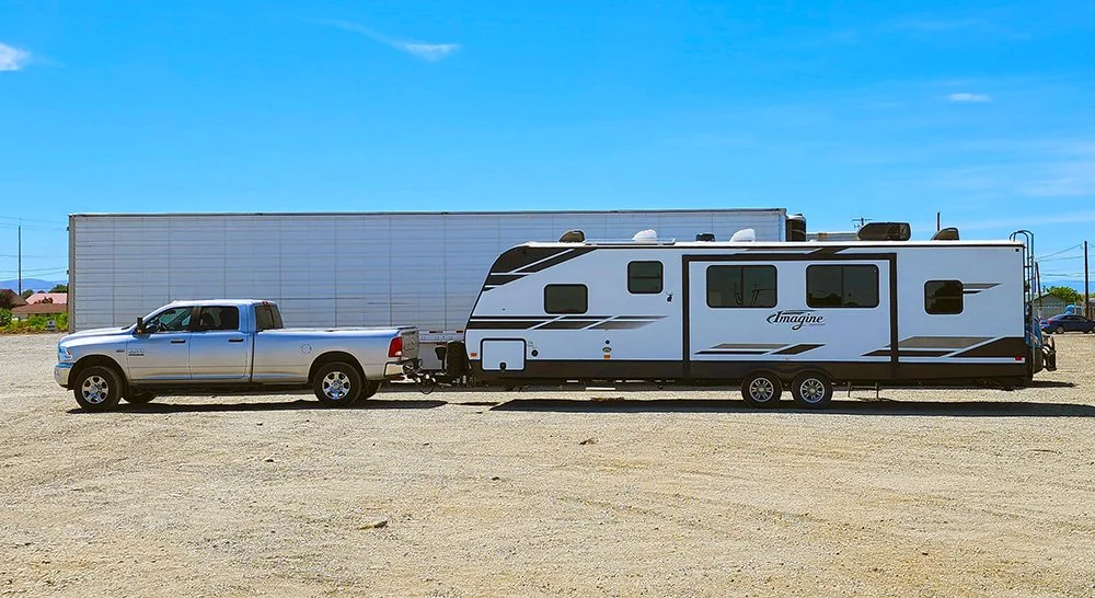 A Ram 2500 towing a Grand Design Imagine RV poses in front of a semi-truck.