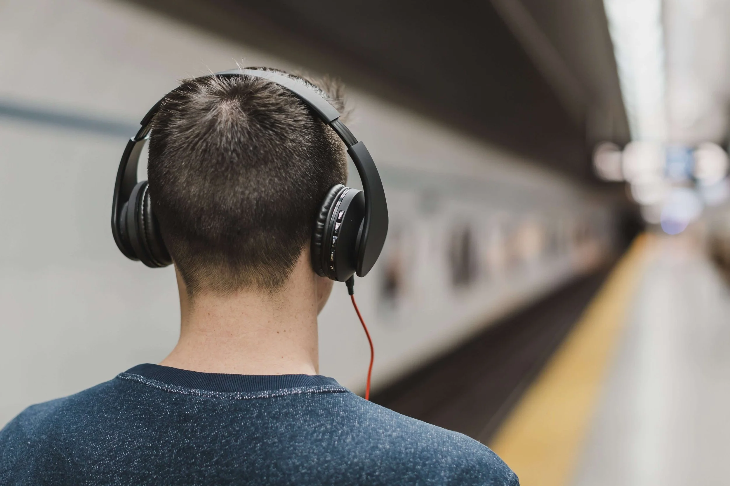 Back of a person wearing headphones at a subway station platform.