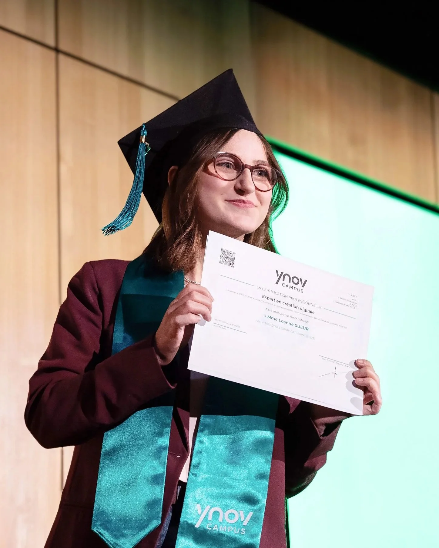 Une femme en tenue universitaire tenant un diplôme lors d'une cérémonie de remise de diplômes.