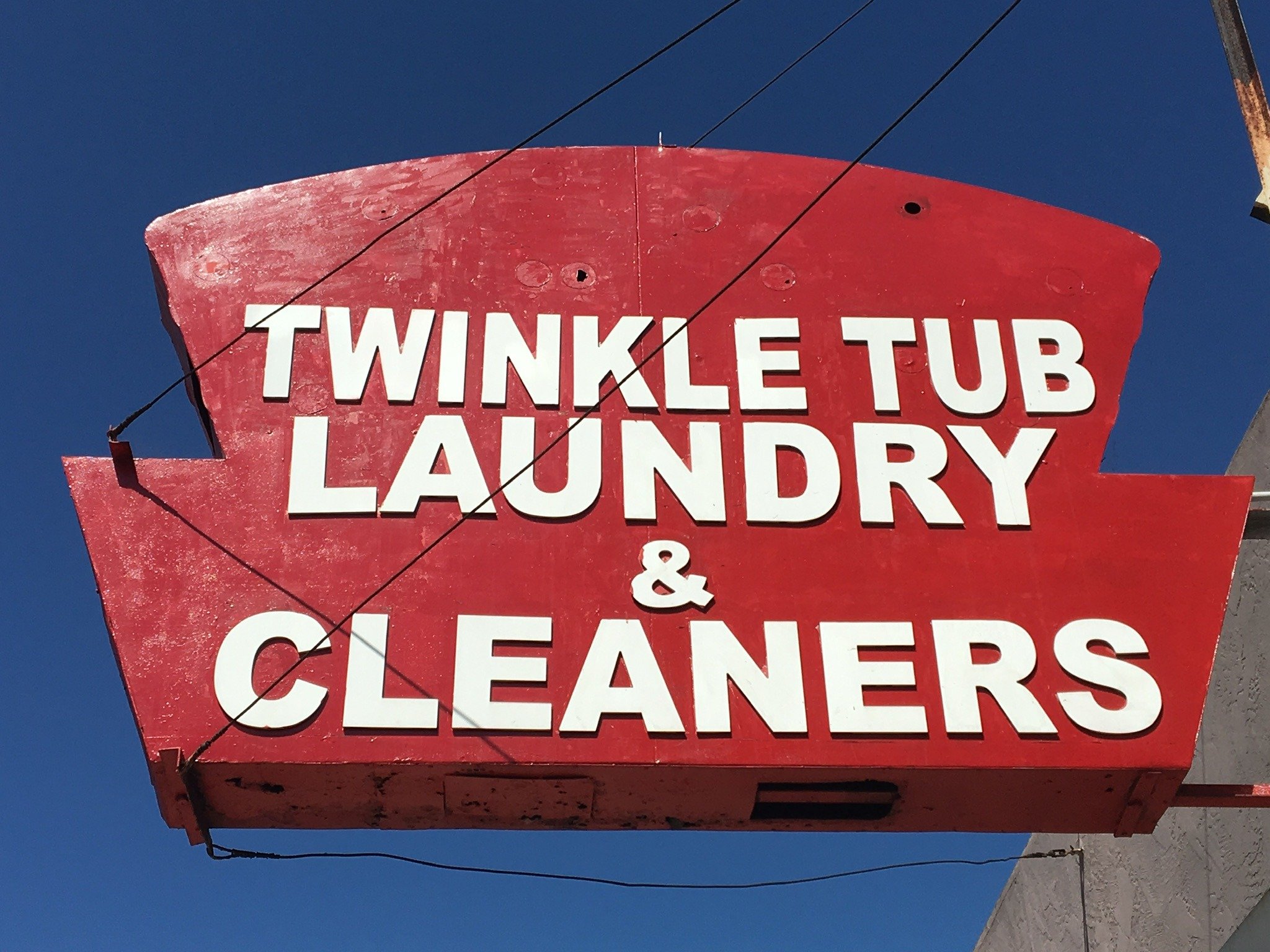 Red vintage sign advertising Twinkle Tub Laundry and Cleaners against a blue sky.