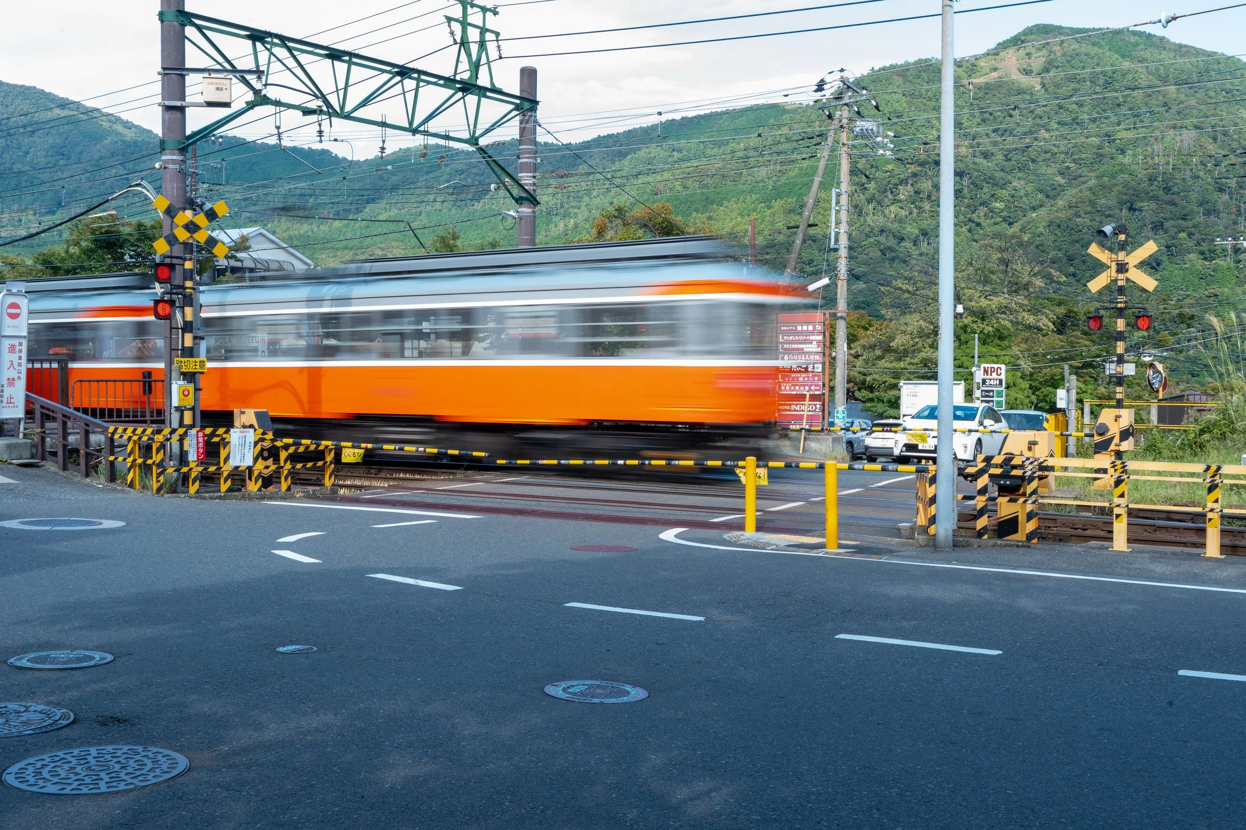 A moving train crossing a railroad crossing on a suburban street with cars and traffic signals, hills and trees in the background.