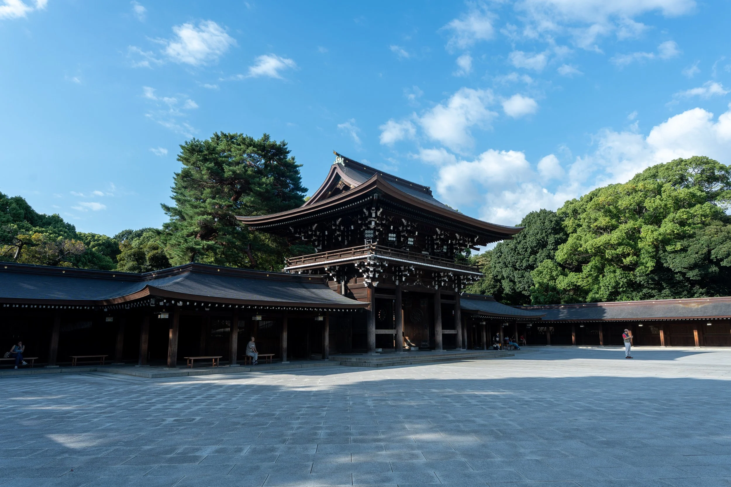 Traditional Japanese wooden building surrounded by green trees under a blue sky with some clouds.