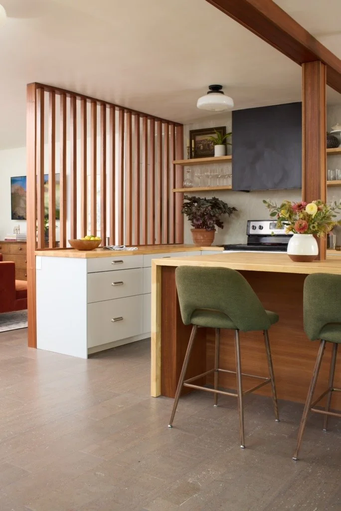 Kitchen with wooden bar stool, potted plant, open shelves, black stove, and wooden accents.