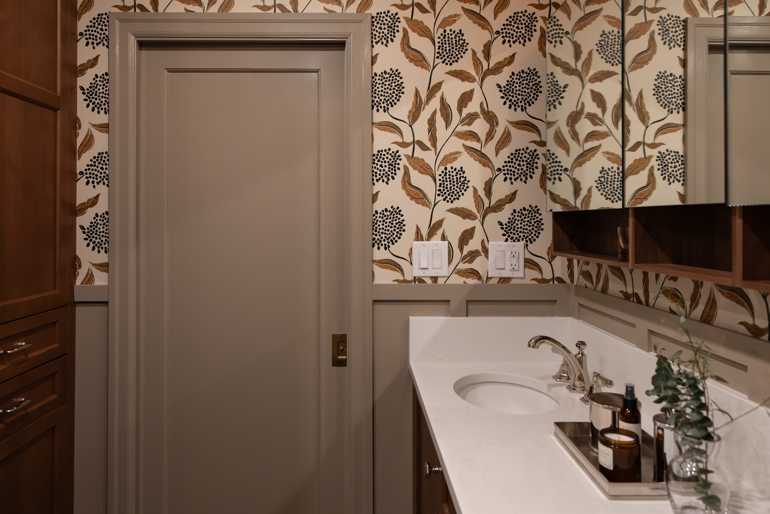 A bathroom with a floral patterned wallpaper, a white countertop with a sink, and wall-mounted mirrors.