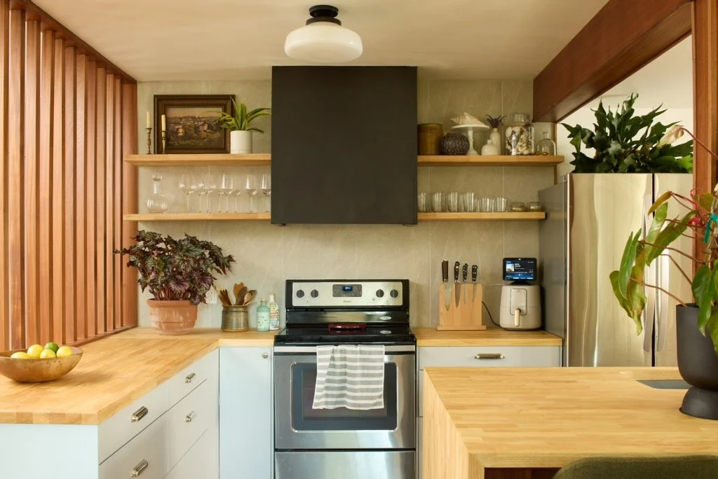 Kitchen with wooden countertops, open shelves with glassware, plants, and a stainless steel refrigerator.