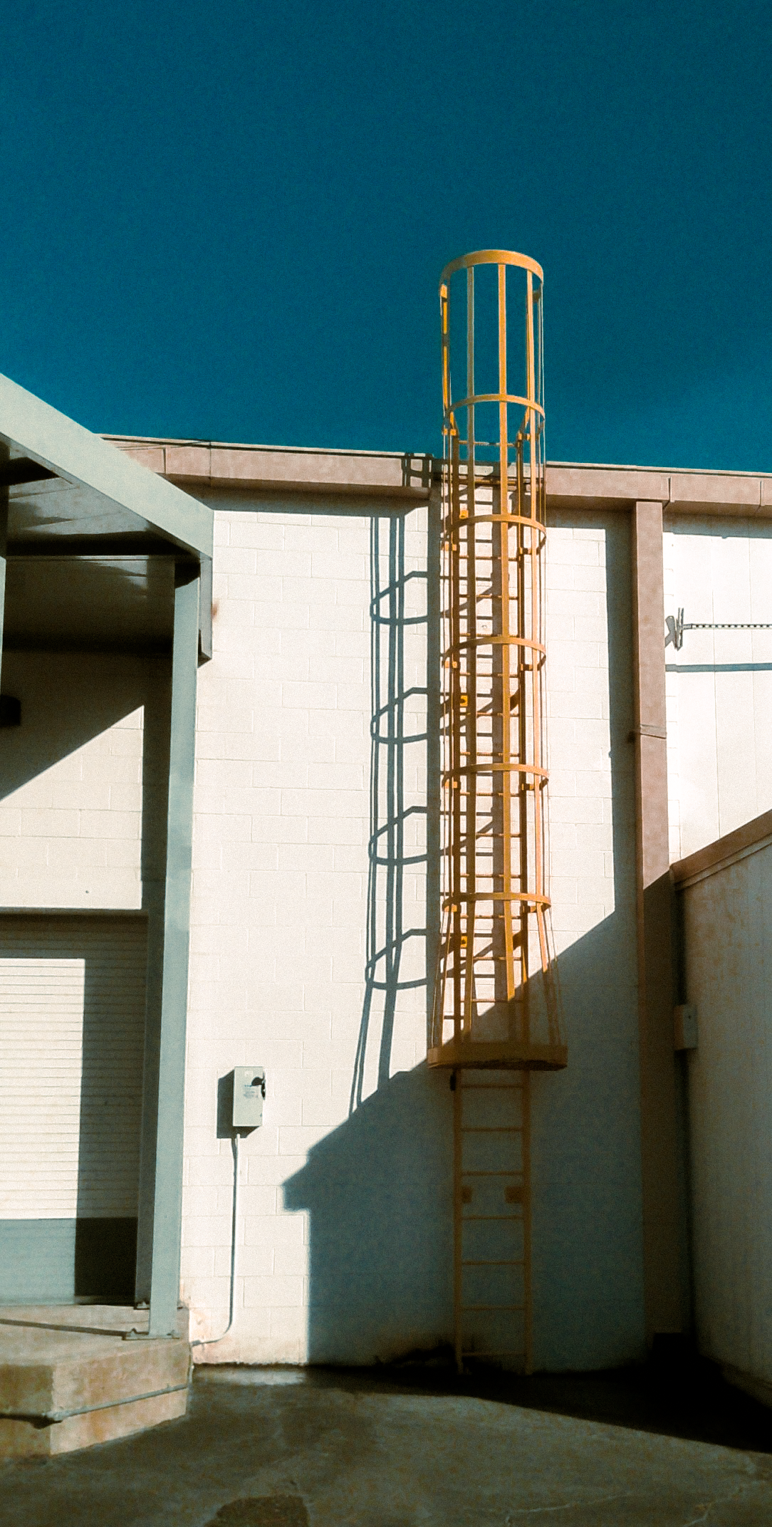 Yellow metal industrial fire escape ladder attached to a white building with a clear blue sky background.