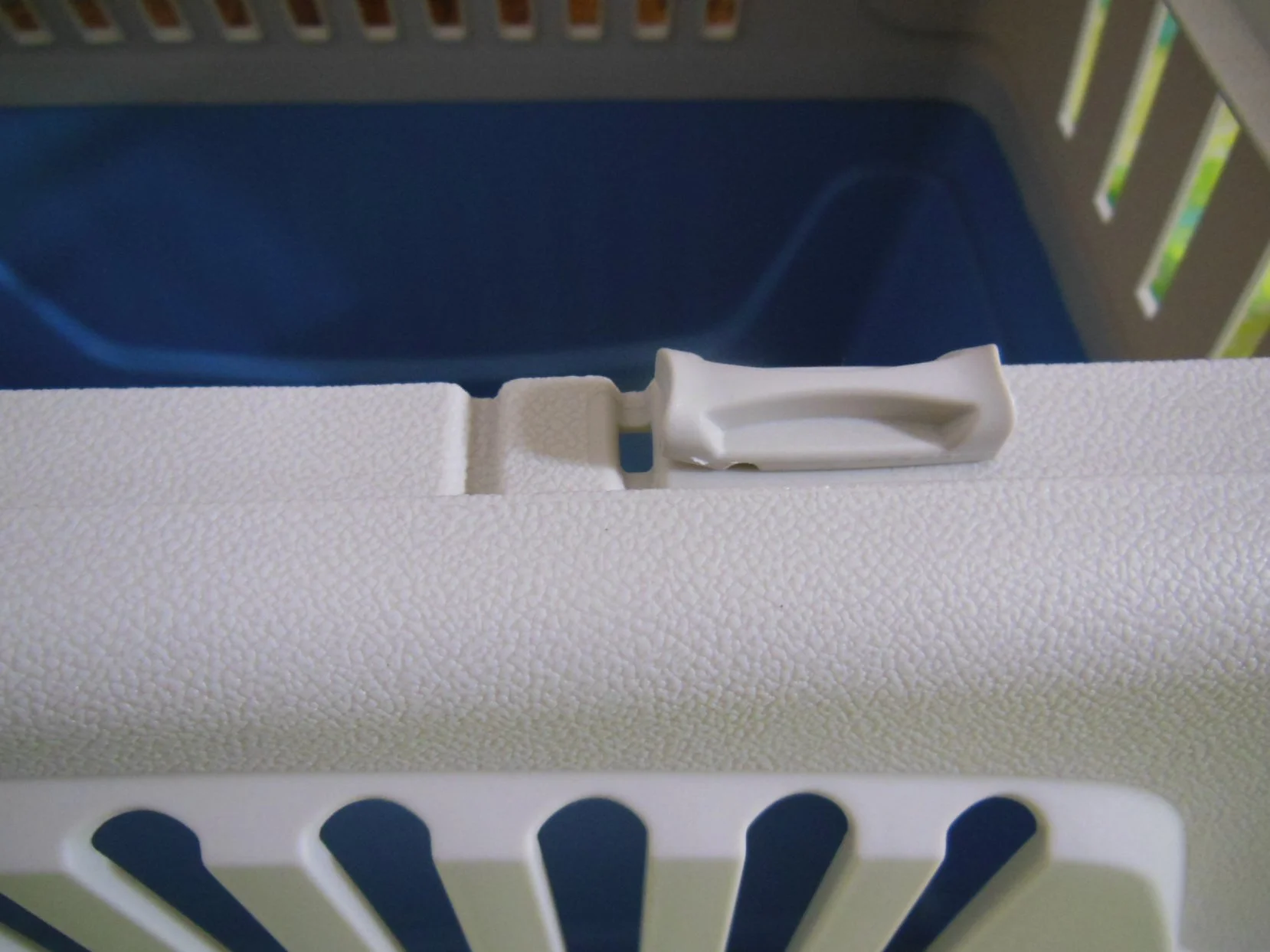 Close-up of a white plastic latch on the top of a white pet carrier with blue interior and vent slats.