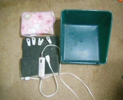 A collection of items on a beige surface, including a pink cloth with white rabbits, a set of white cables with tags, a green cloth, a small white device attached to the cable, and a large empty teal container.