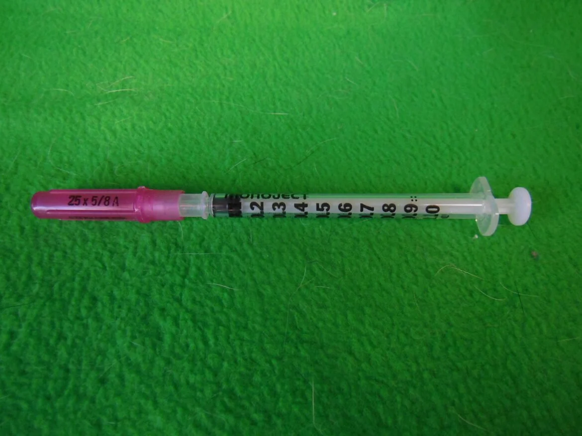 A medical syringe with a pink needle cap lying on a green textured surface.