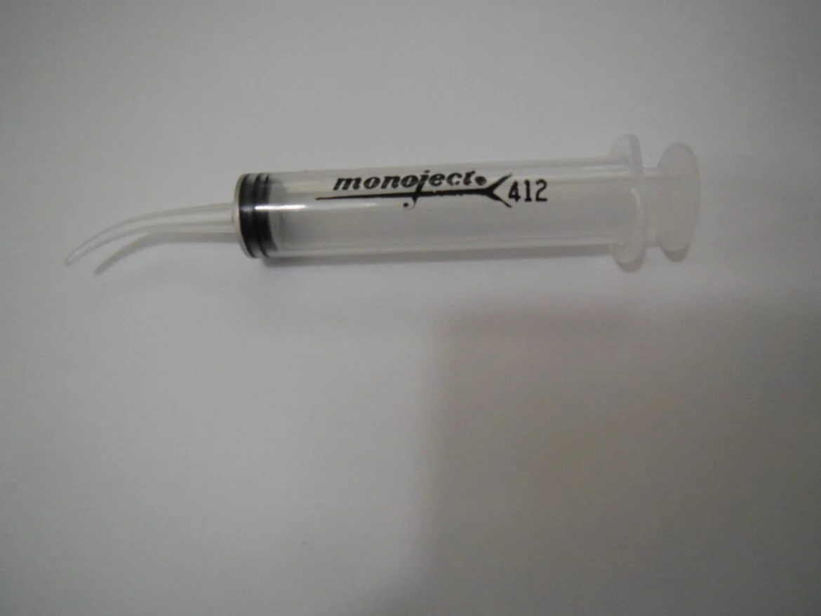 A clear syringe with black markings lying on a white surface.