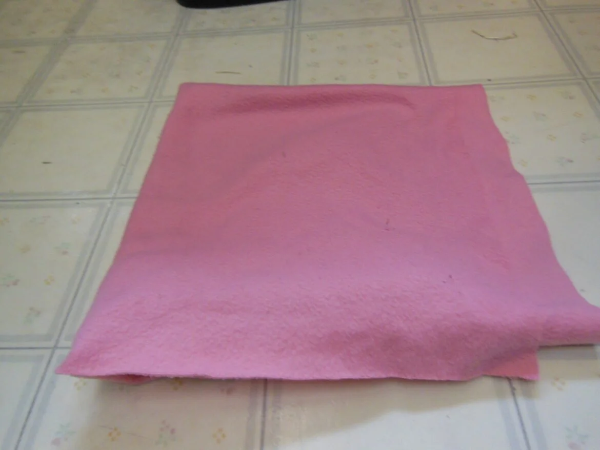 A pink towel laid flat on a tiled floor.