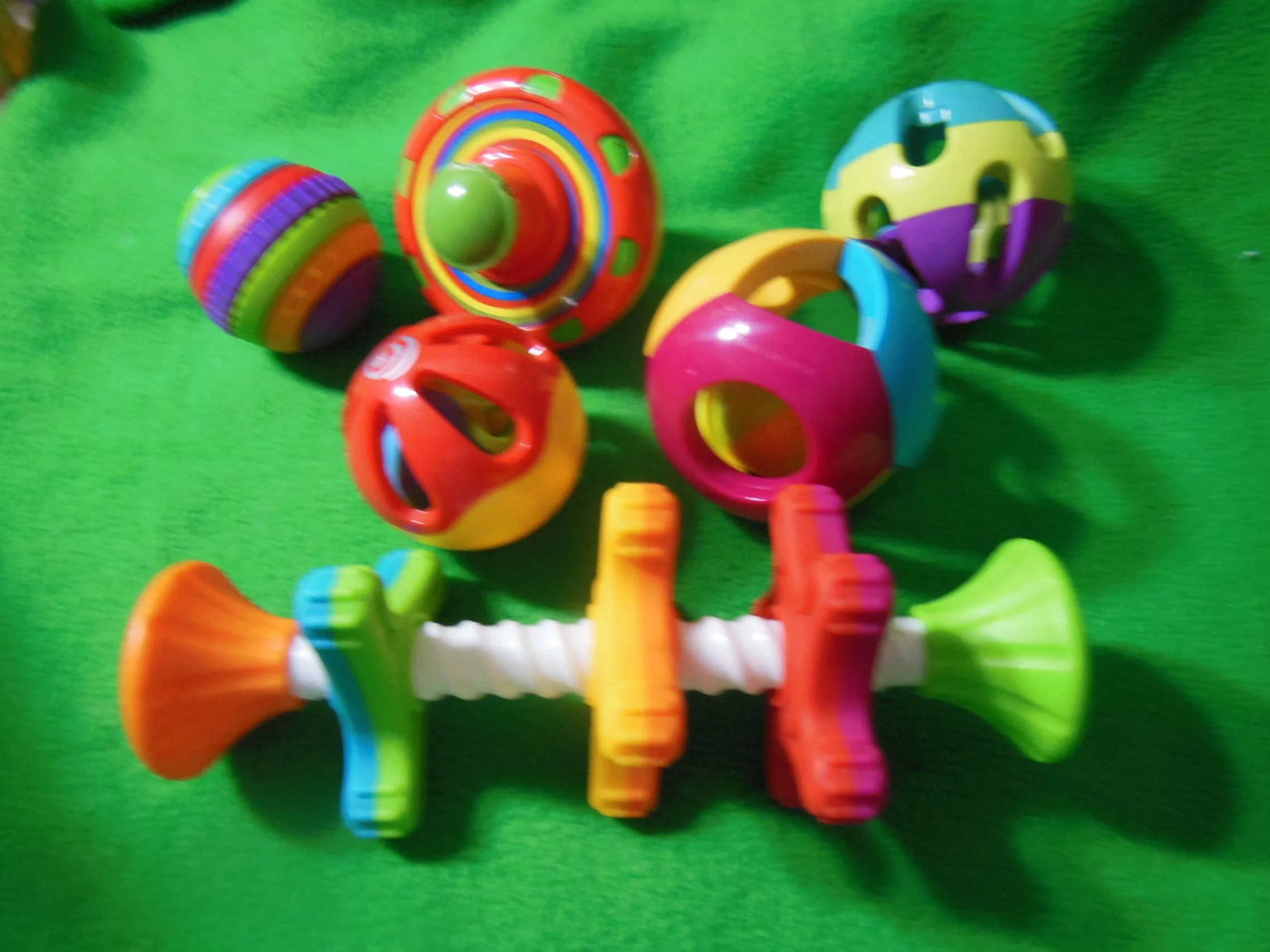 Colorful plastic baby rattles and balls on a green surface.