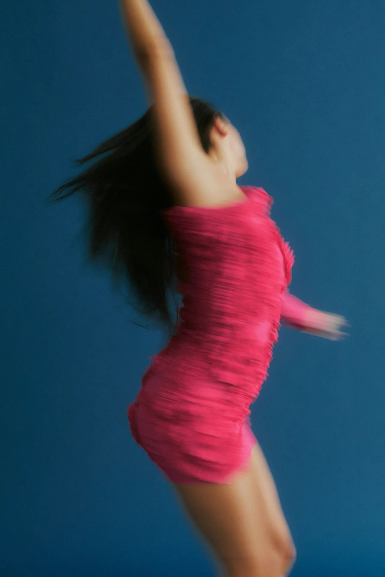 A woman in a pink dress dancing against a blue background.