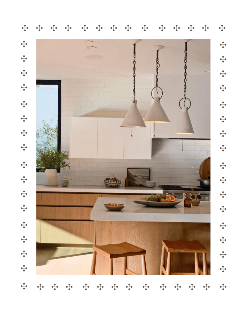 Modern kitchen with white cabinets, pendant lights, a white countertop island with wooden stools, and decorative bowls and plants.