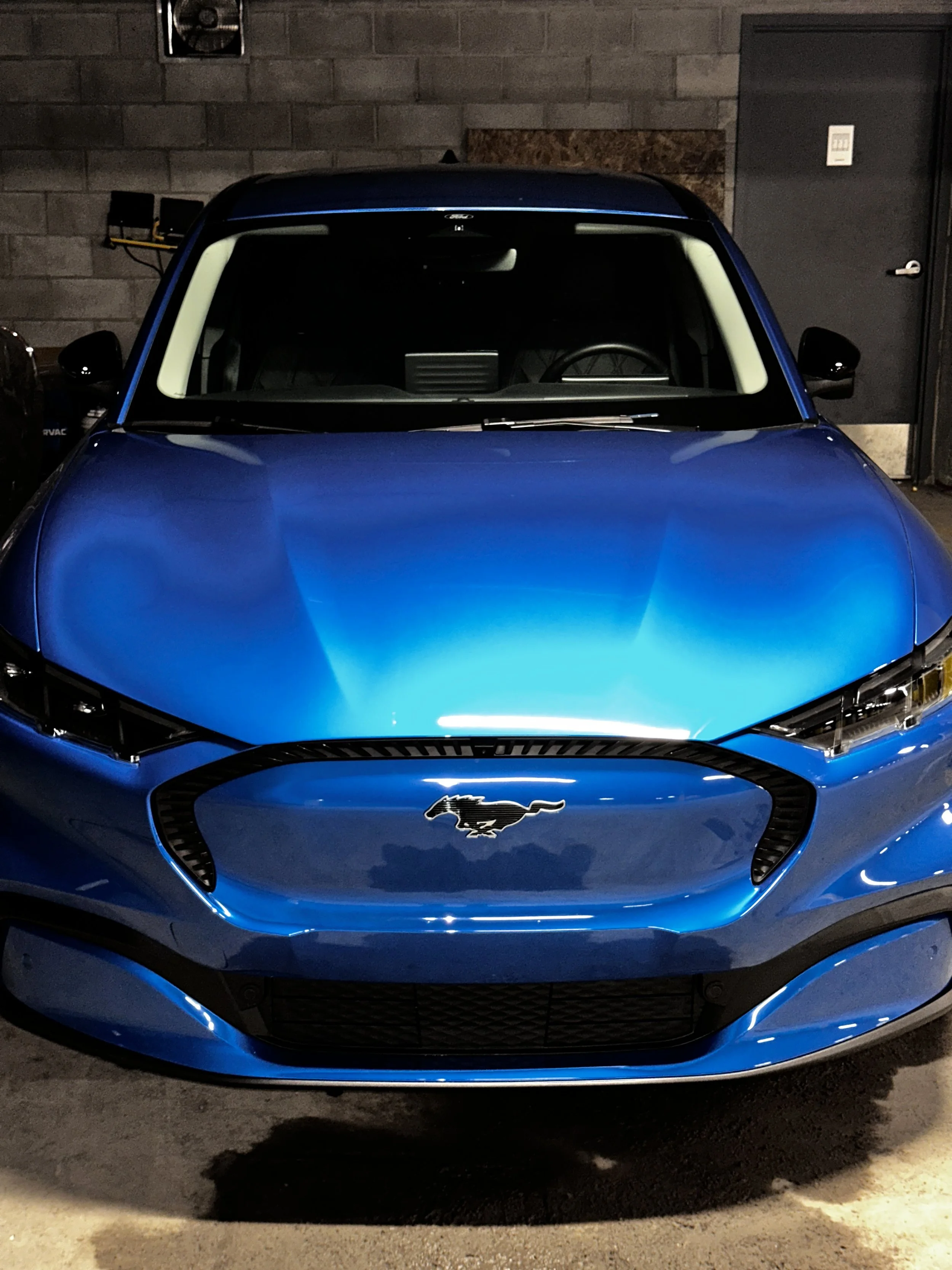 Blue Ford Mustang electric vehicle in a dimly-lit garage.