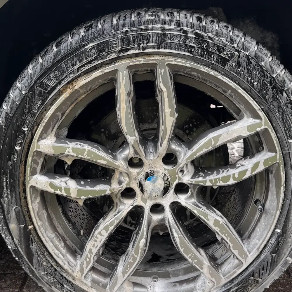 Close-up of a car wheel with a rim, covered in soap suds during a car wash.
