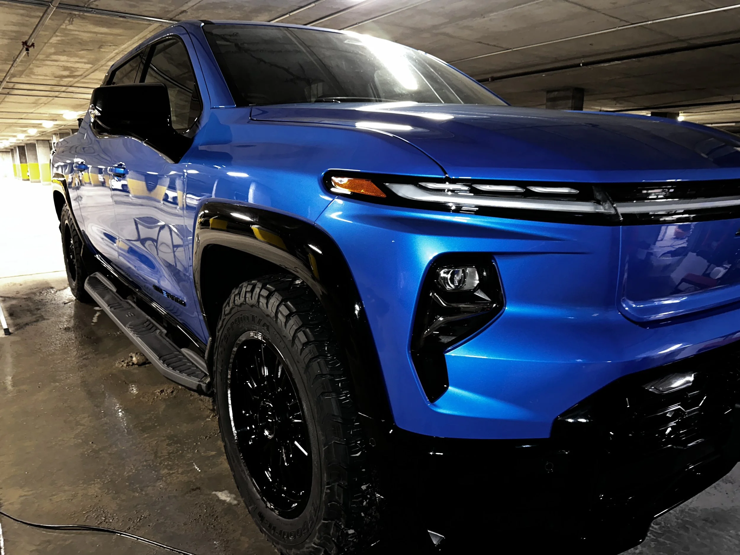 A blue modern pickup truck with black accents parked in an indoor parking garage.