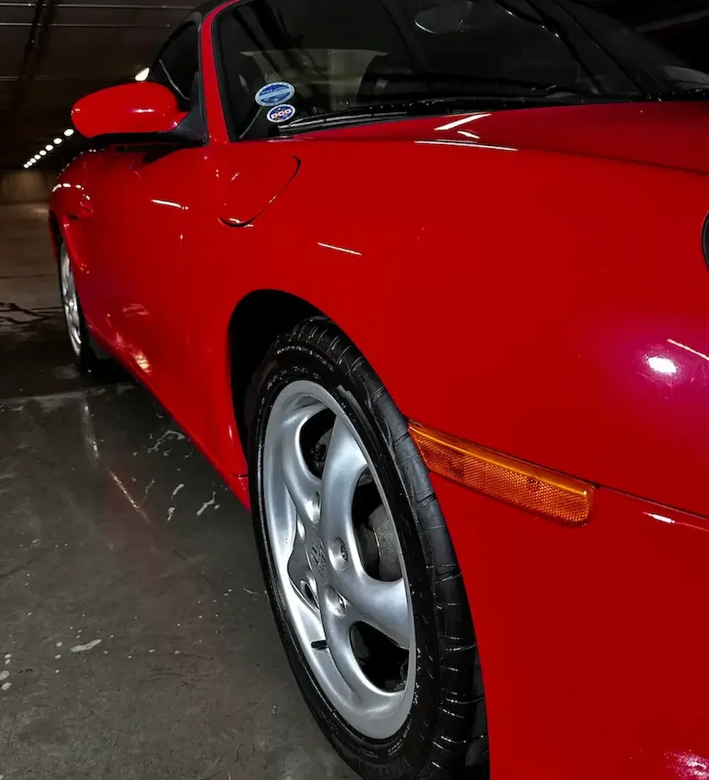 porsche parked in an indoor garage, showing the front left side with a tire and part of the door and side mirror.
