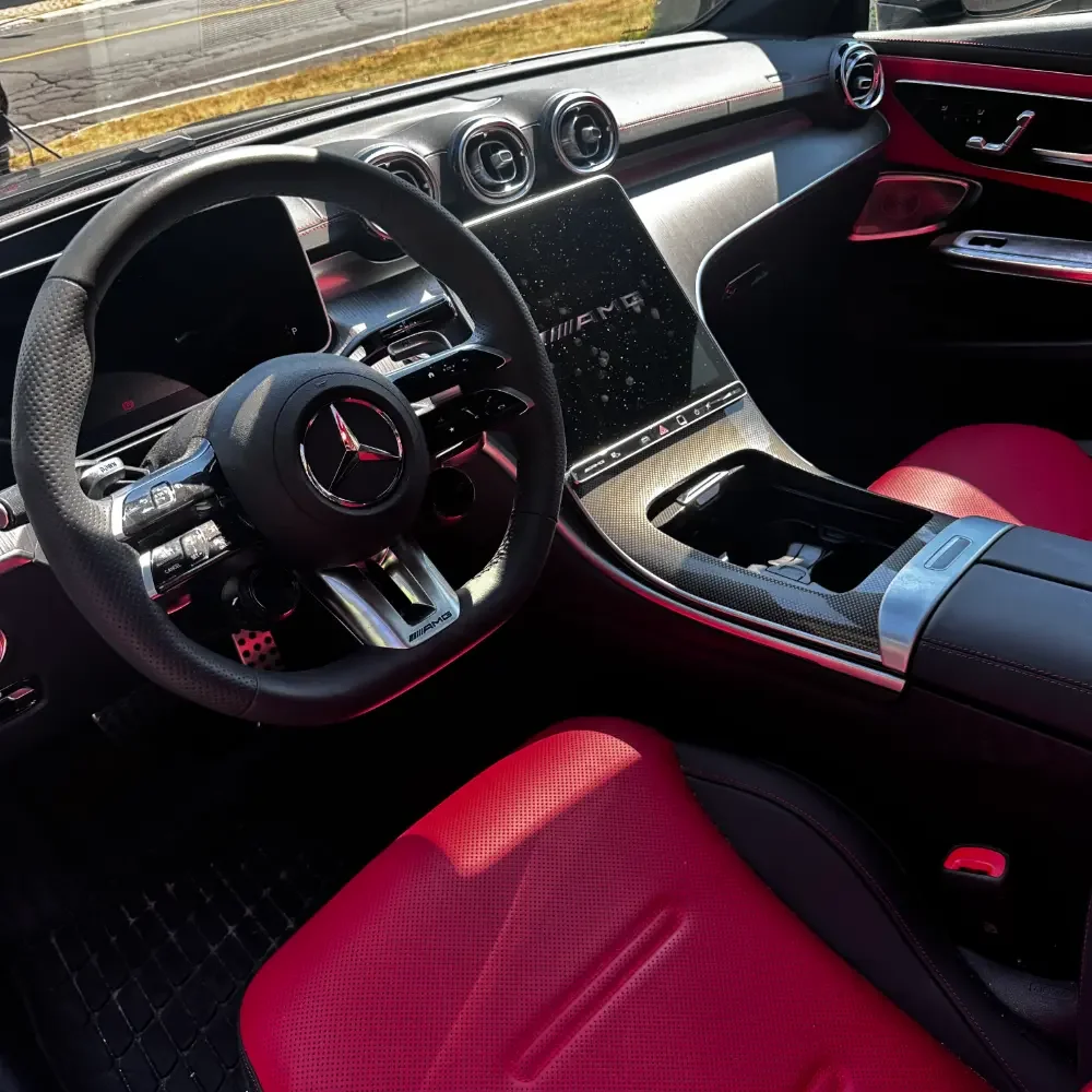 Interior of a Mercedes-Benz AMG car with a steering wheel, dashboard, and red and black seats.