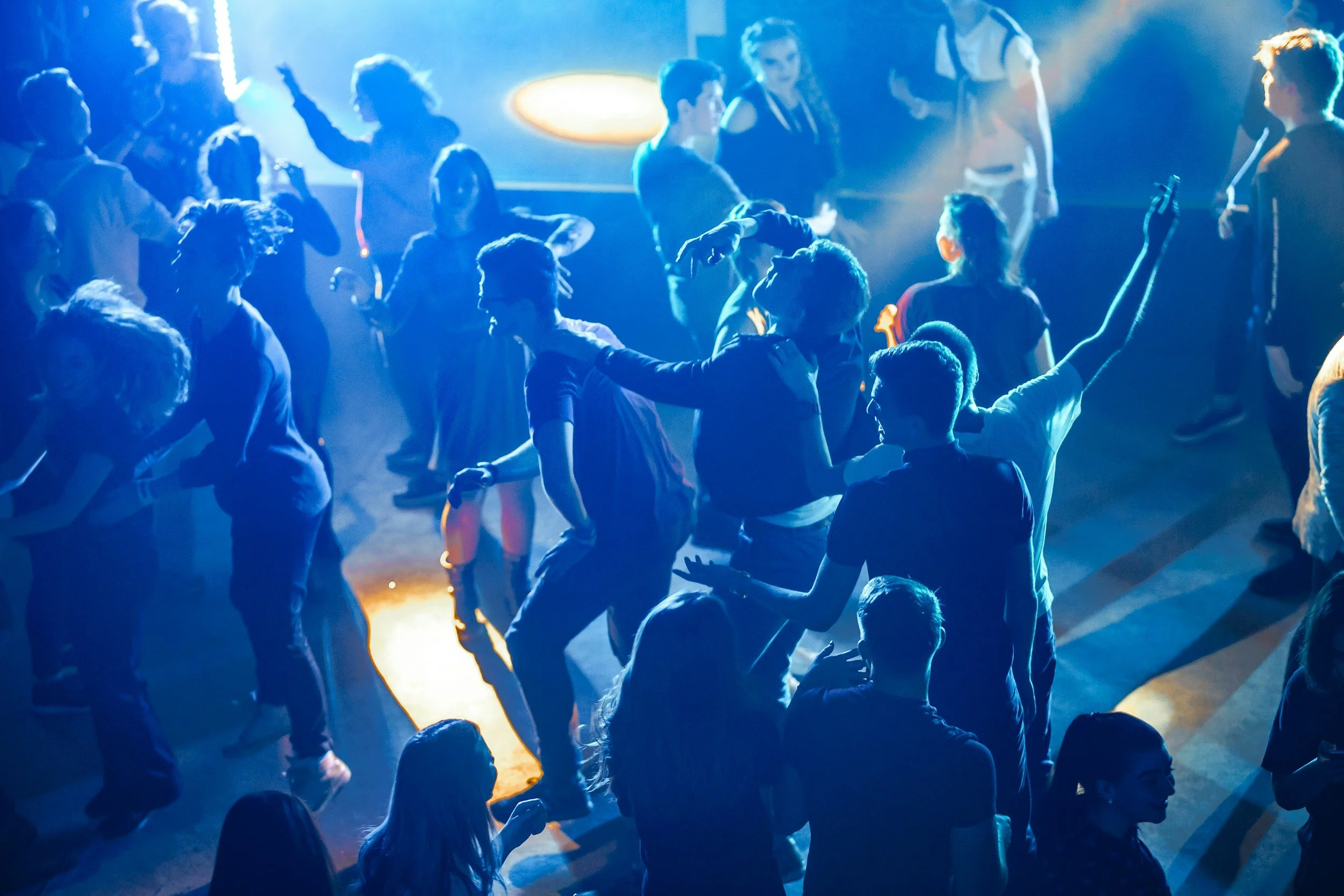 Group of people dancing and socializing at a nightclub with blue and yellow lighting.