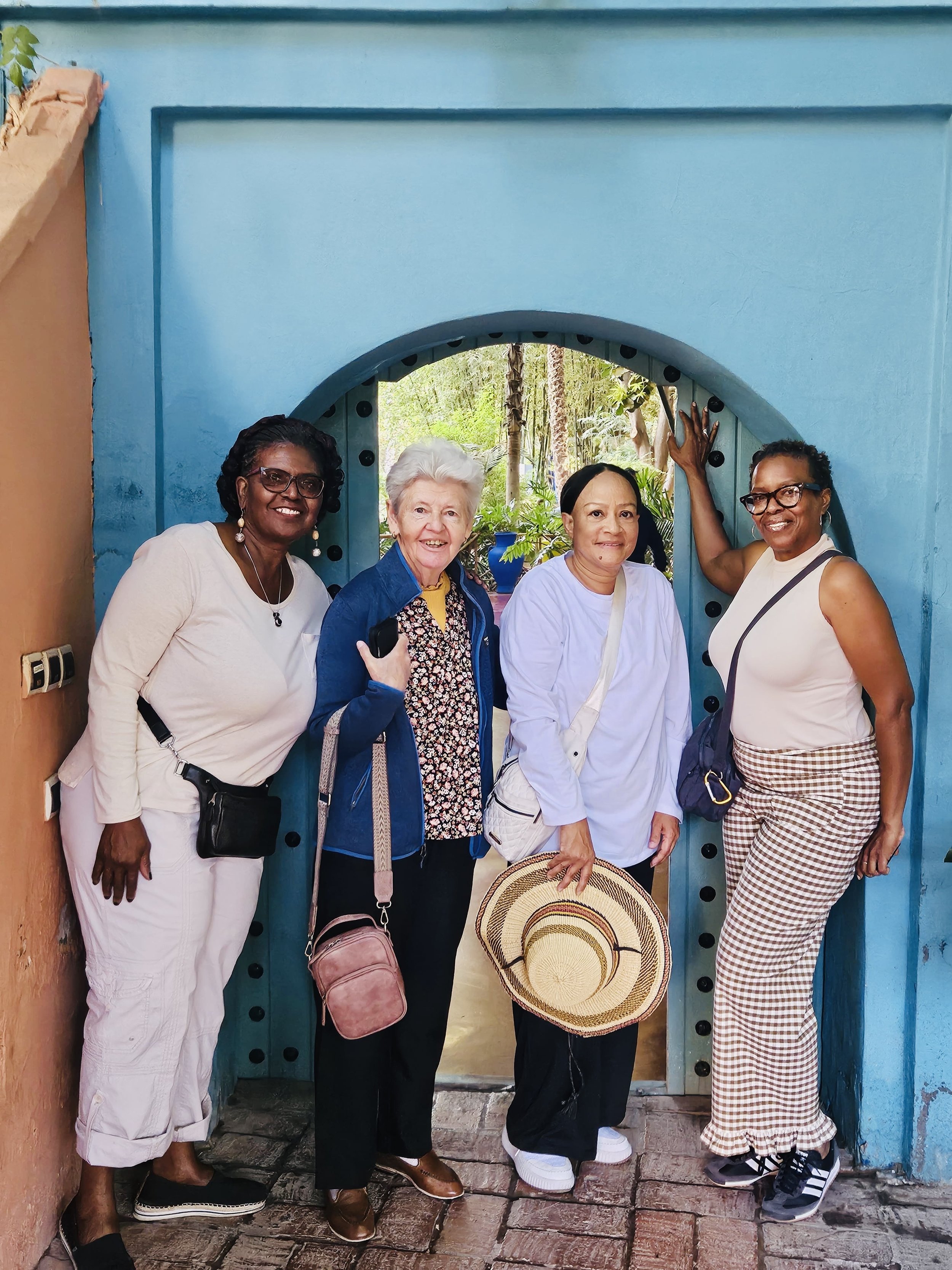Four women standing at a blue door with a circular opening, smiling for the photo.