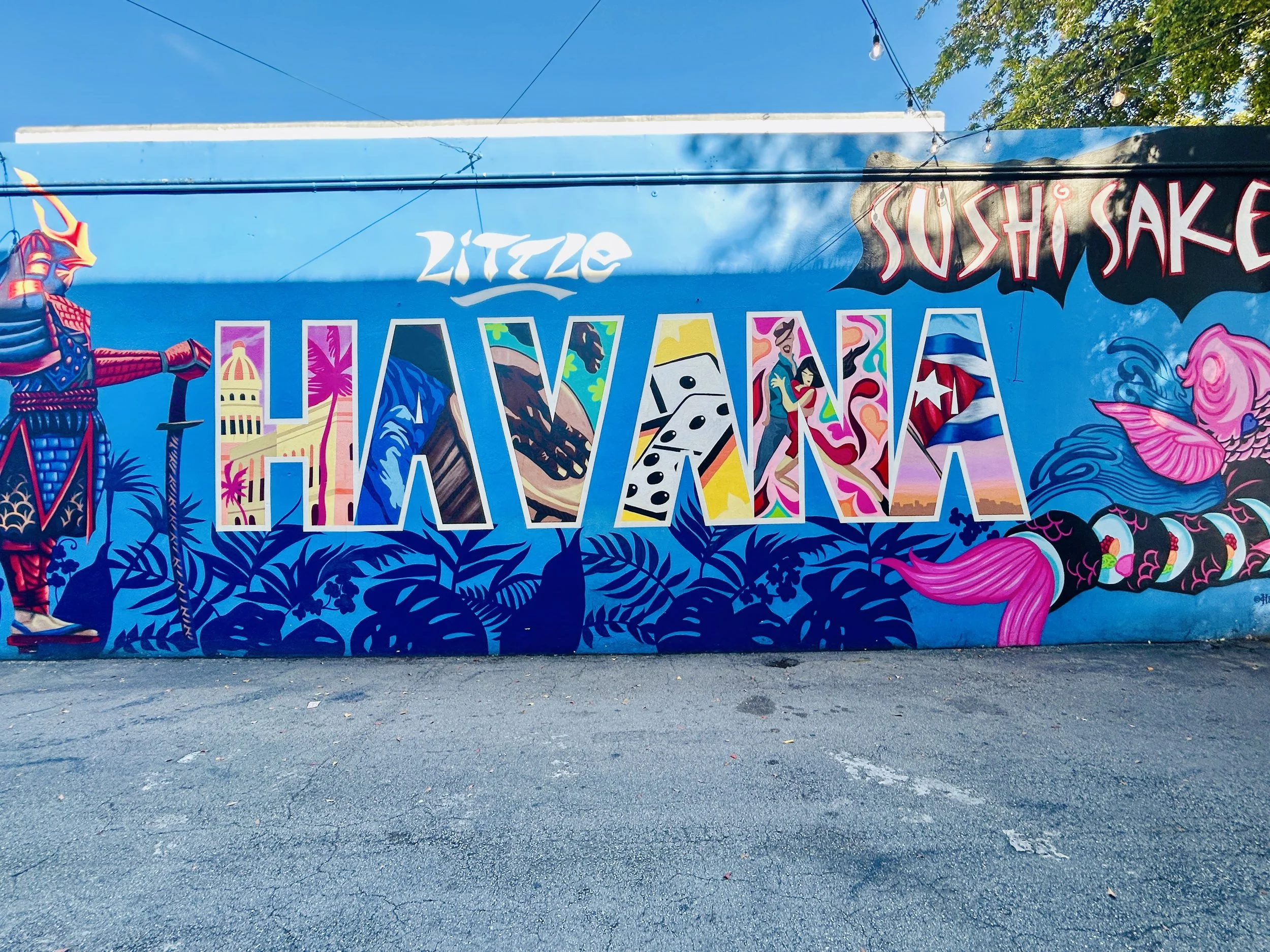 Colorful mural art on a wall featuring the word 'Honolulu' in large, stylized letters filled with scenic and cultural images representing Hawaii, including Aloha shirts, surfboards, traditional clothing, and island scenery, with additional text 'LITT