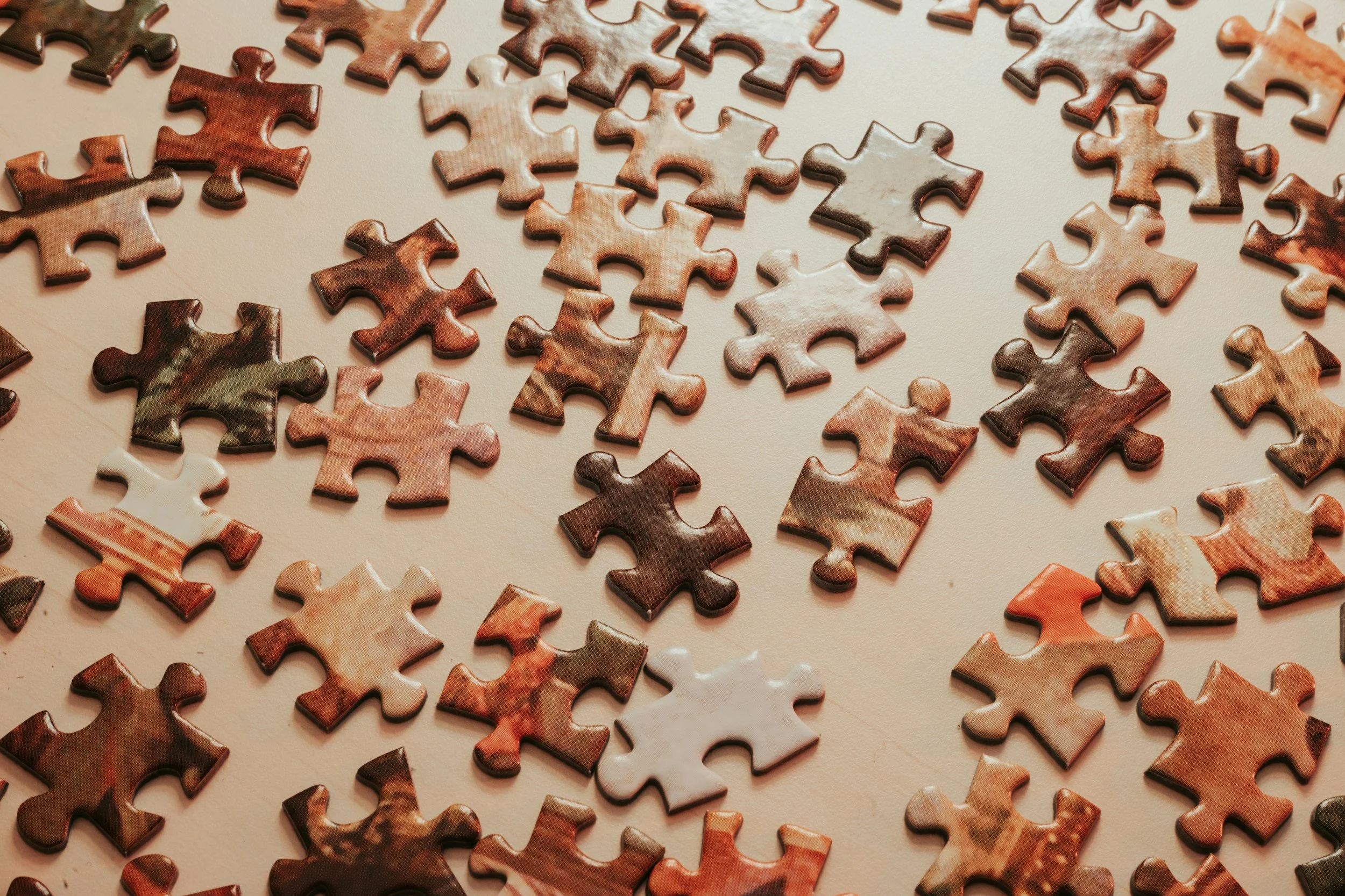 A scattered collection of puzzle pieces with varied earthy, brown, and beige tones, some with marbled or textured patterns, laid out on a light-colored surface.