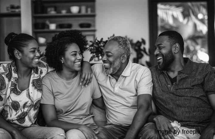 A multi-generational family sitting closely on a couch, smiling and enjoying each other's company in a cozy living room.