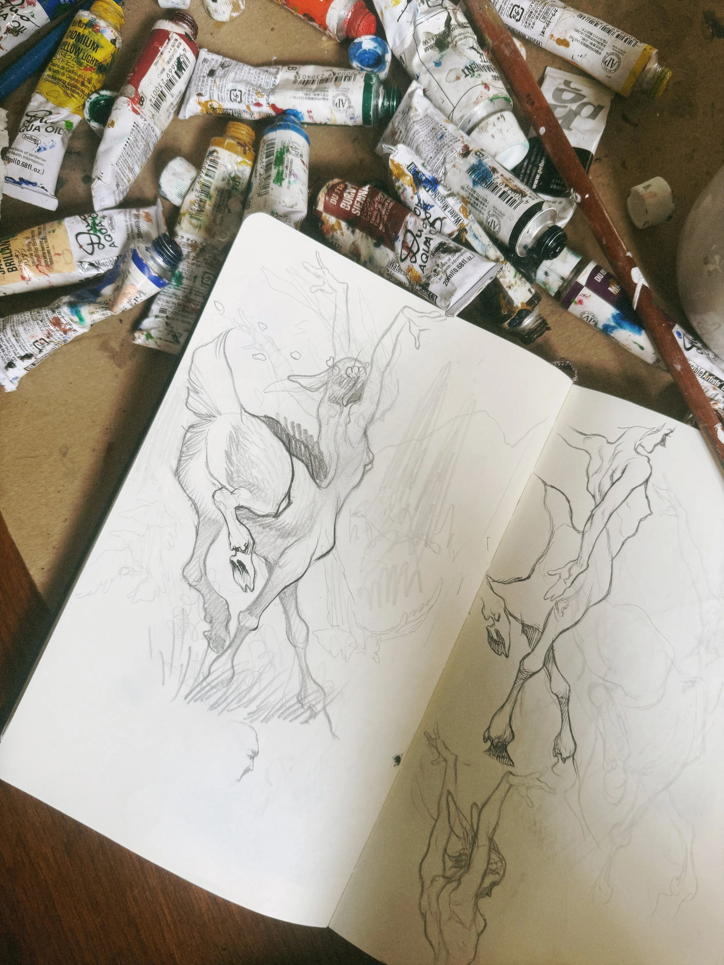 Drawing of a horse on paper surrounded by paint tubes and art supplies.