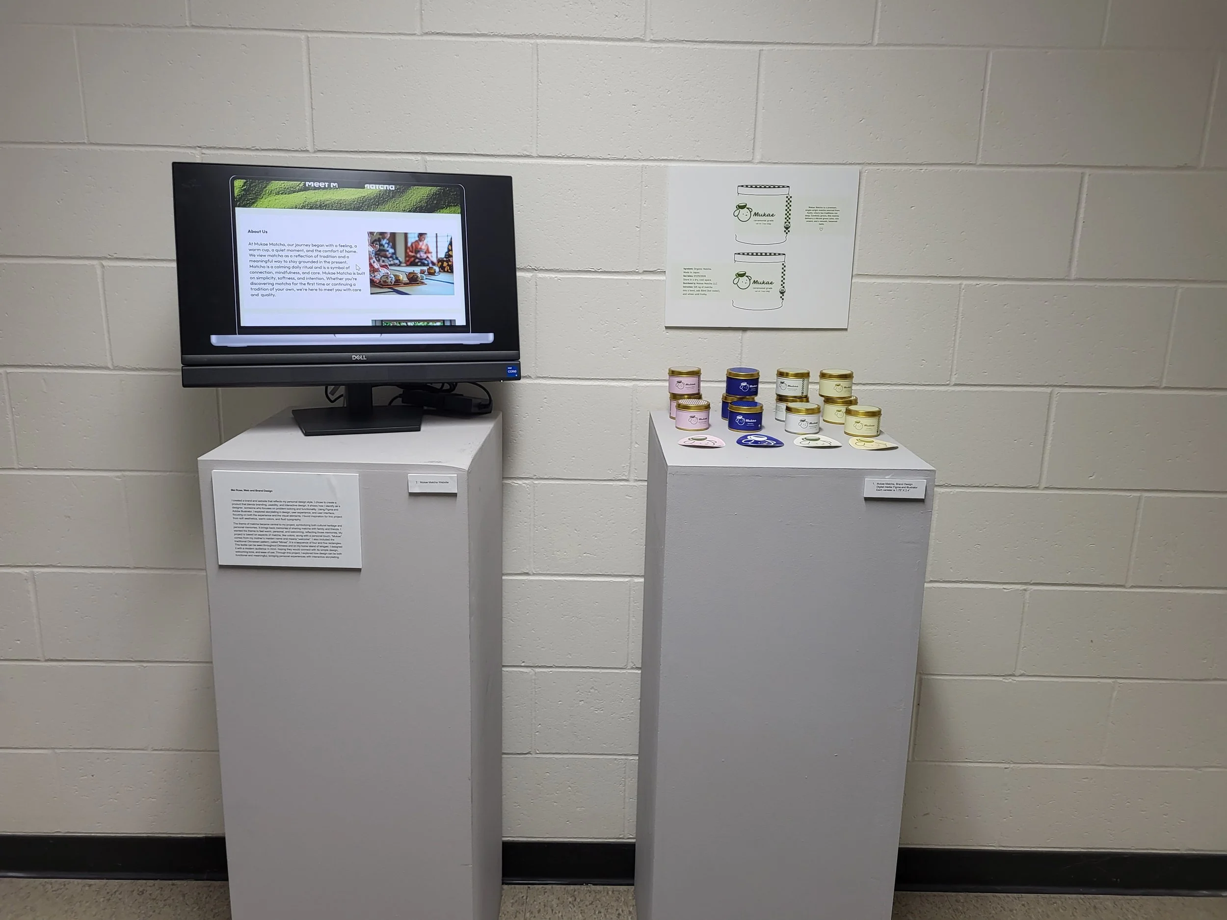An exhibit display featuring a computer monitor on a white pedestal, with a diagram of jars on the wall behind, and small jars of various colors on a white pedestal to the right, against a white brick wall.