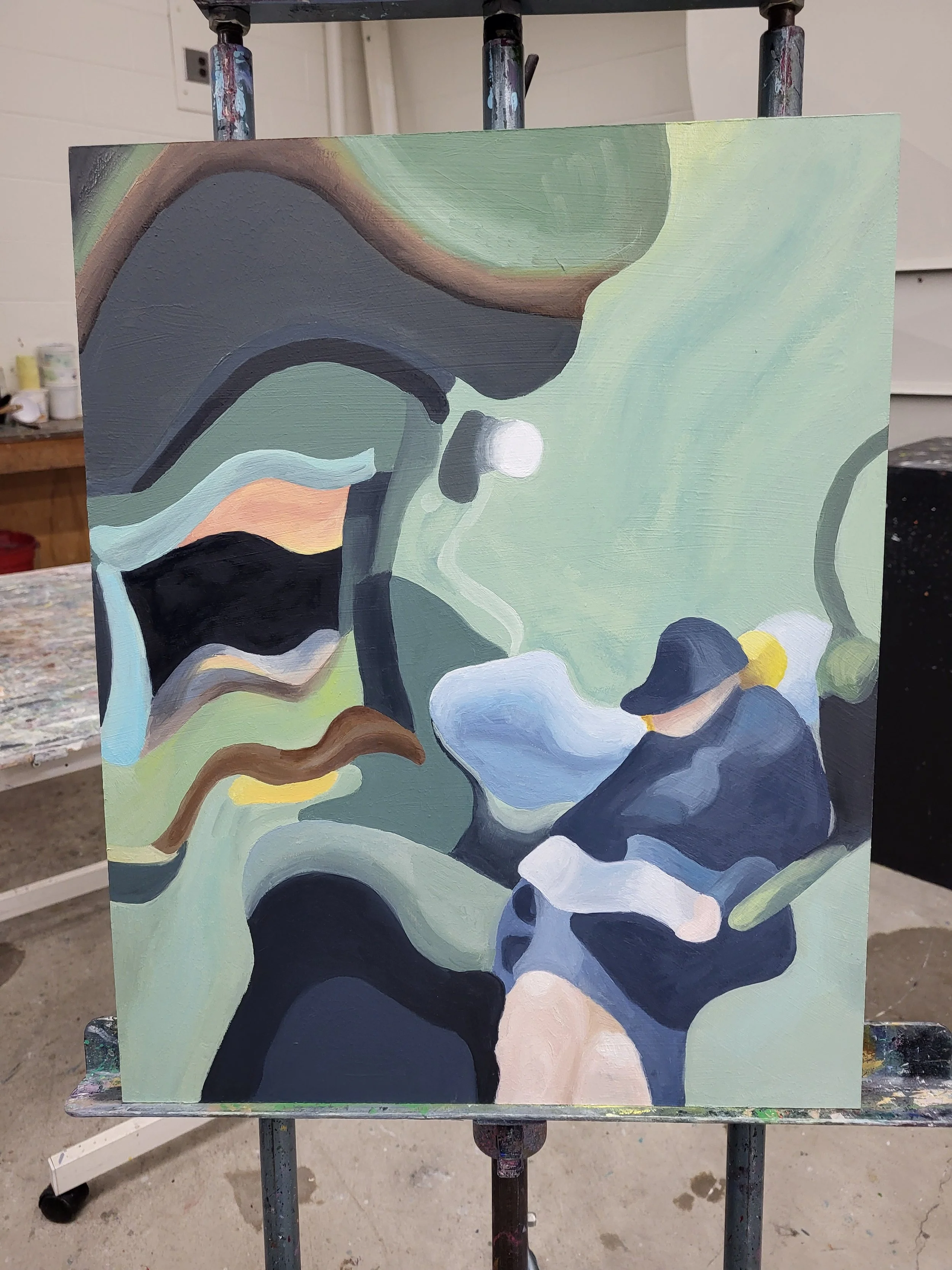 Abstract painting with various curved and flowing shapes in shades of green, black, white, and touches of peach, yellow, and blue, on a canvas on an easel in an art studio.