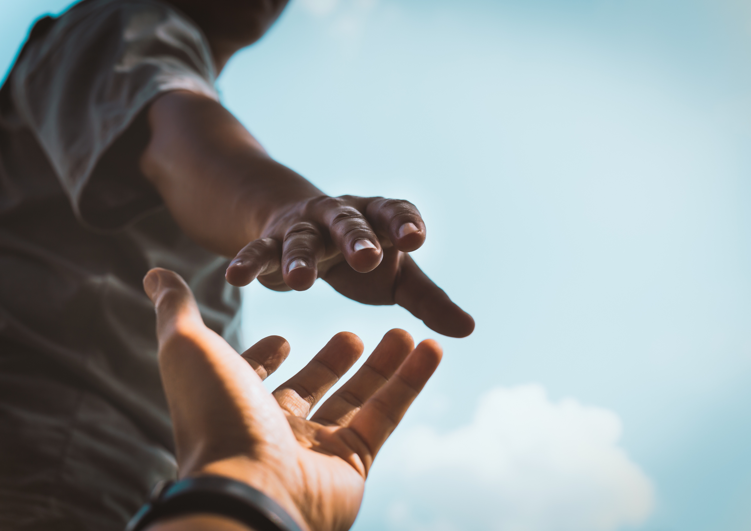 A person reaching down and helping another person up, with a cloudy sky in the background.