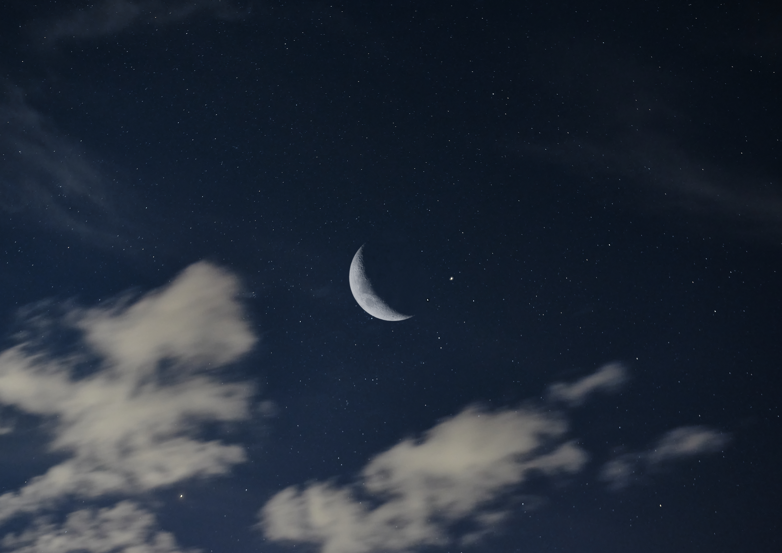 Night sky with a crescent moon, stars, and some scattered clouds.
