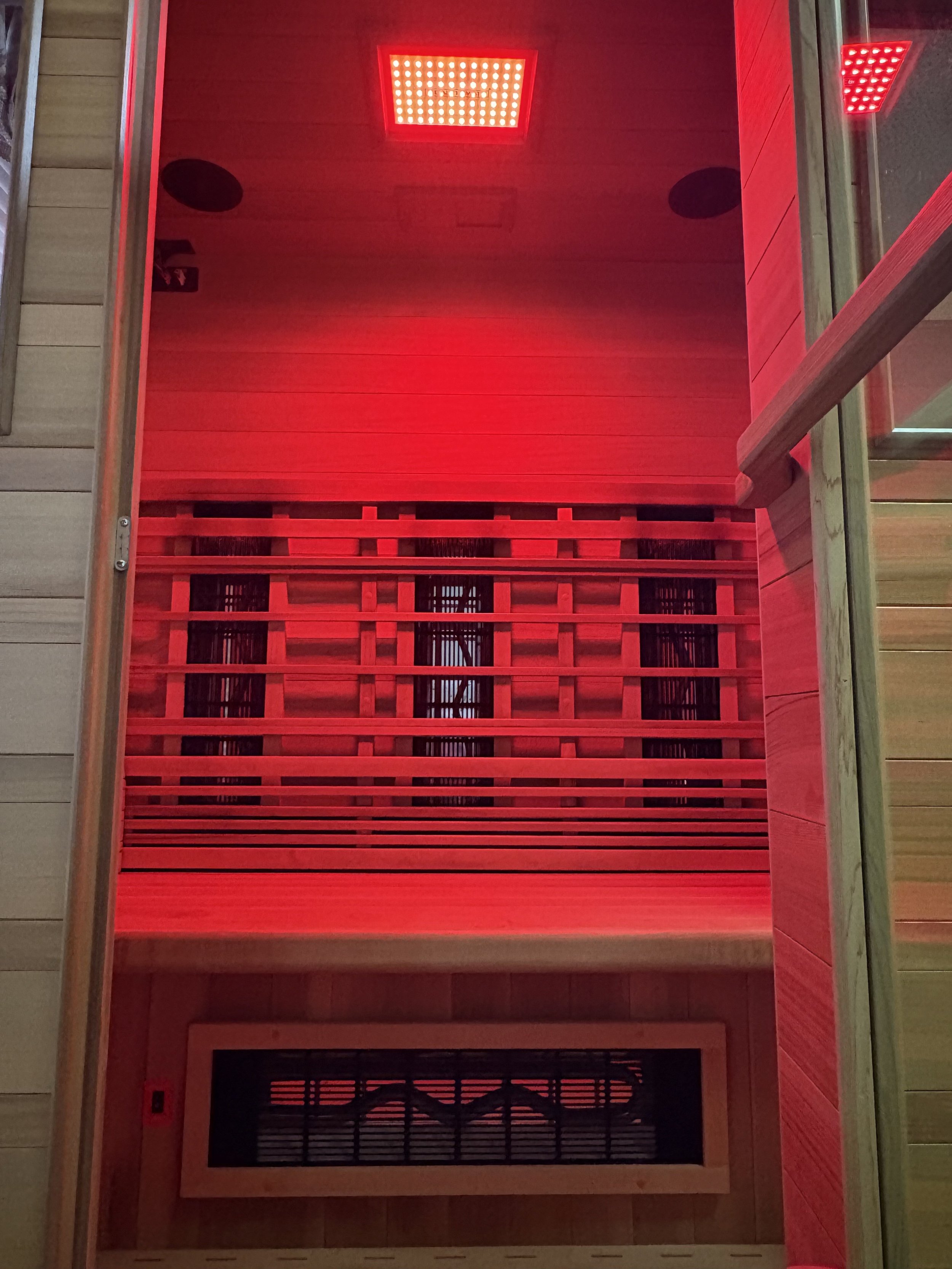 Interior view of a sauna with red lighting, wooden slats, and a small window at the bottom.