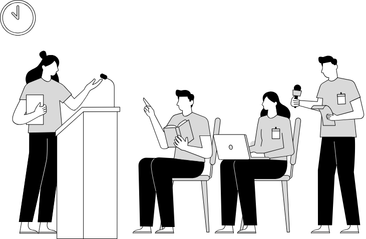 A presenter stands at a podium speaking to three seated individuals with laptops and notes during a meeting or conference.