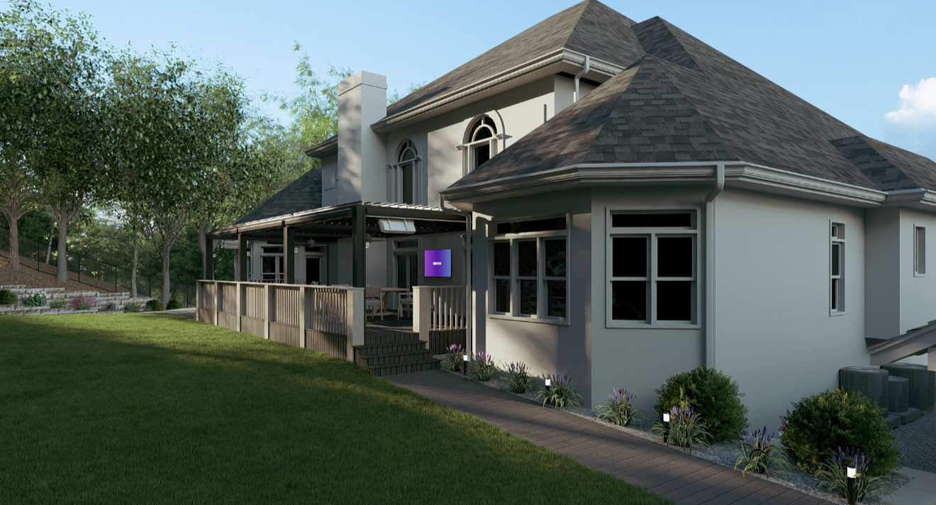 A two-story house with a large deck, surrounded by greenery and trees, featuring multiple windows and a sloped roof.