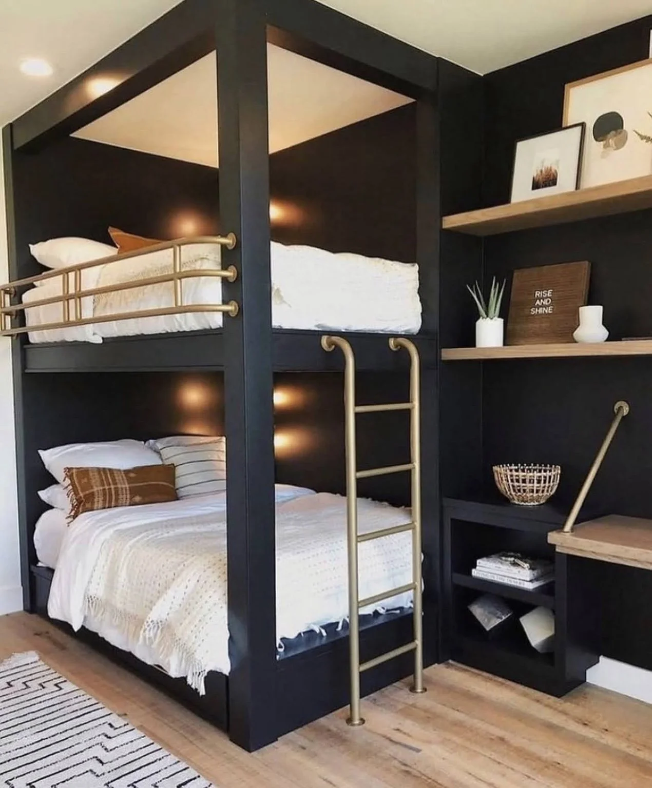 Matte-black custom bunk room with brass rails and ladder, warm wood surfaces, and an integrated desk.