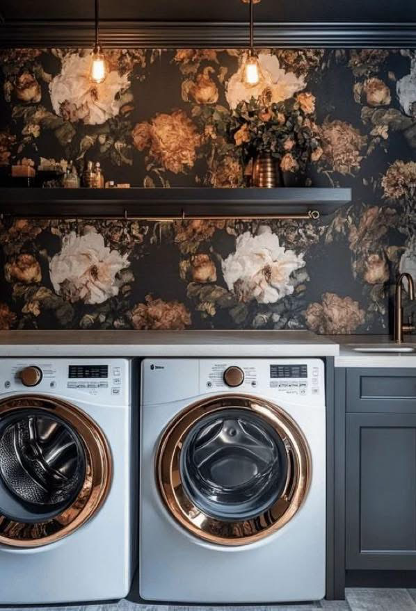Floral laundry room with oversized botanical wallpaper, dark cabinetry, warm pendant lights, and front-loading laundry appliances.