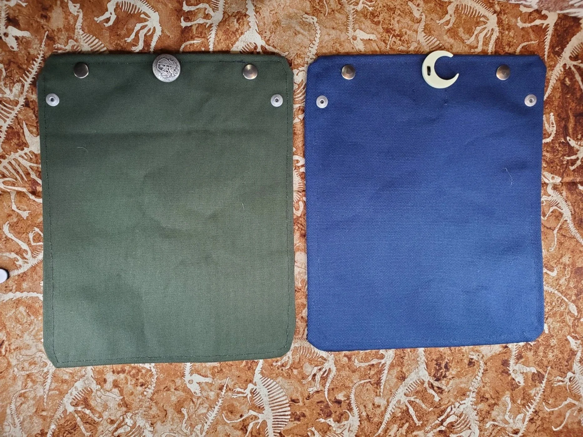 The outside of 2 Dice Rolls. One in green canvas with a pewter button and the other in navy canvas with a moon shaped acrylic button.