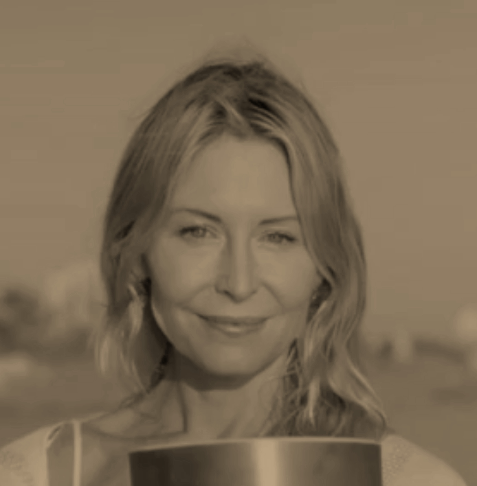 A woman with wavy long hair smiling outdoors, with a blurred background.